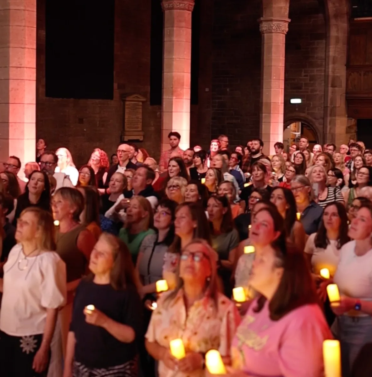 A packed hall singing by candlelight